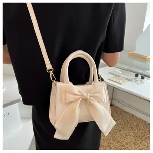 Chic beige small crossbody bag featuring a large tulle bow decoration shown on a model