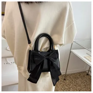 Close-up of black crossbody bag with large mesh bow and gold hardware on model