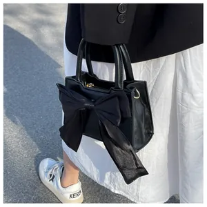 Detail of black leather handbag featuring a large tulle bow decoration and metal hooks