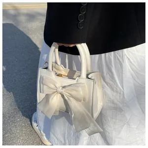 Detail view of a cream white handbag featuring a large organza bow and dual top handles