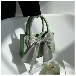 Detail of light green faux leather handbag featuring a large grey organza bow decoration