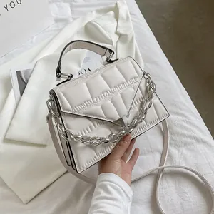 Close-up of off-white quilted handbag with chunky silver chain and triangular metal buckle