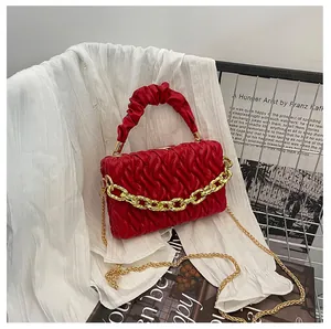 Detail view of red matelassé handbag with gold chain strap on soft white fabric
