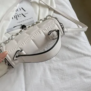 Close-up of white matelassé cylinder shoulder bag with silver chain and vogue magazine accessory