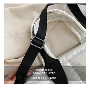 Detail of adjustable black fabric shoulder strap with silver metal buckle on white puffer bag