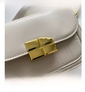 Detail of cream flap shoulder bag featuring gold textured lock and crocodile pattern