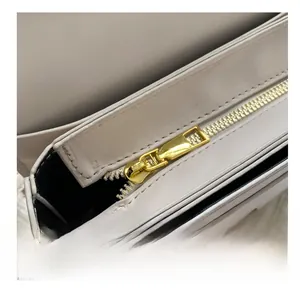 Close-up of a smooth gold metal zipper on a premium cream white leather handbag detail