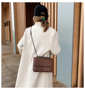 Rear view of a model wearing a brown quilted leather crossbody bag with chain strap
