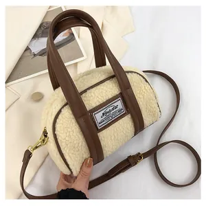Close-up of beige plush Boston bag with brown leather handles and brand logo tag