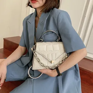 Detail of white crocodile pattern handbag with silver metal handle and chain strap on model