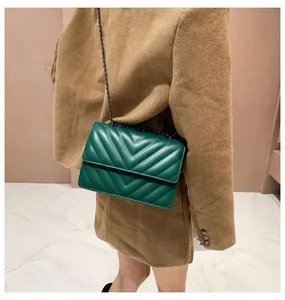 Detail of dark green V-quilted leather bag with black metal chain strap on model