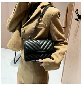 Detail of black V-quilted flap shoulder bag with grey chain strap on female model