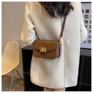 Close-up of a brown crossbody bag with gold buckle and crocodile texture on tweed coat