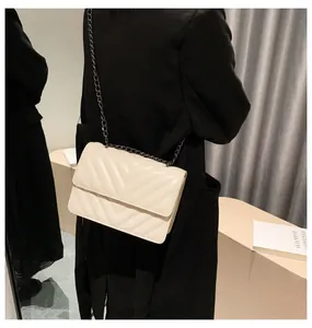 Detail of cream quilted crossbody bag with dark grey metal chain on a model