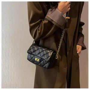Detail of a black quilted leather crossbody bag with gold chain strap on a trench coat