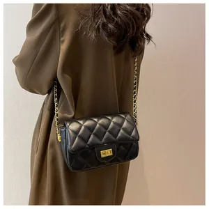 Detailed view of black quilted leather shoulder bag with golden chain on dark trench coat