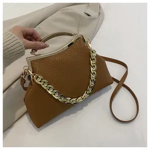 Detail van bruine reliëf lederen tas met gouden sluiting en ketting op beige blazer