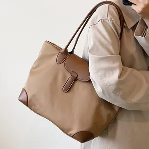 Minimalist khaki canvas tote bag with brown leather trim shown on shoulder with trench coat