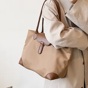 Large khaki nylon tote bag with brown leather trim carried by a model in a trench coat