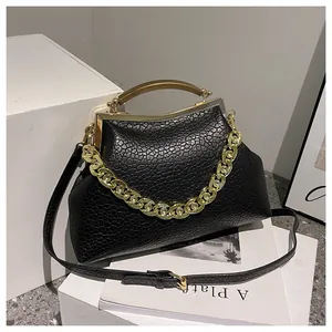 Detail van zwarte tas met krokodillenmotief, gouden handvat en ketting op witte blokken