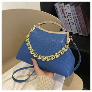 Detail van blauwe crossbodytas met steenpatroon, gouden ketting en metalen handvat
