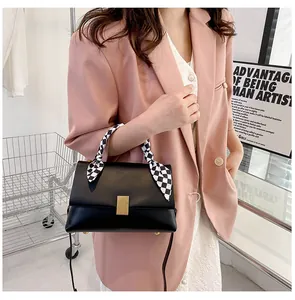 Détail d'un sac à main en cuir noir avec boucle dorée et foulard en soie à carreaux au manche