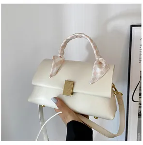 Détail d'un sac à main blanc crème avec fermoir doré et foulard en soie sur la poignée
