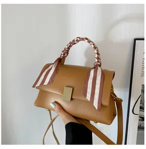 Détail du sac à main en cuir marron avec un foulard en soie rayé enroulé autour de l'anse