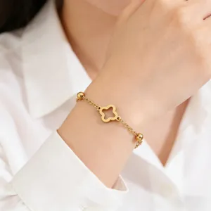 Detail of a minimalist gold clover charm bracelet with small beads on a woman's wrist