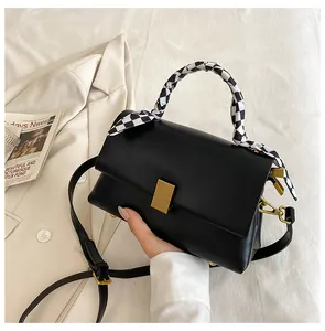 Détail du sac à main en cuir noir avec boucle dorée et poignée ornée d'un foulard à damier
