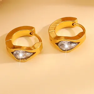 Macro detail of gold huggie earrings featuring a sparkling pear-shaped zircon stone