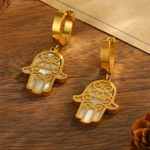 Detailaufnahme der goldenen Hamsa-Hand-Ohrringe mit weißer Muschel und Hohlmuster