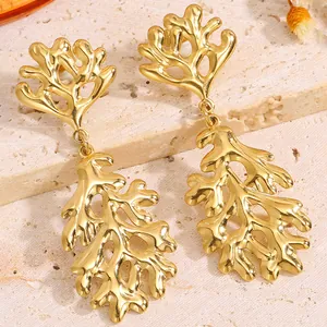 Détail de boucles d'oreilles corail en acier inoxydable doré sur pierre texturée