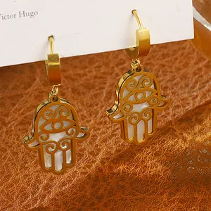 Makroaufnahme goldener Hamsa-Hand-Ohrringe mit weißem Muscheleinleger und Cut-Outs