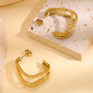 Dettaglio macro di orecchini placcati in oro con trama a corda su sfondo pietra beige