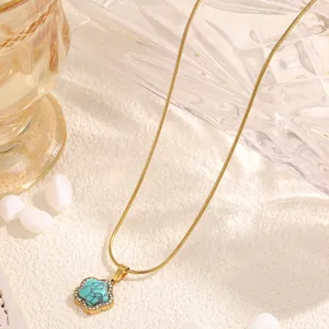 Vue macro du pendentif fleur dorée avec centre turquoise et cristaux sur chaîne serpent