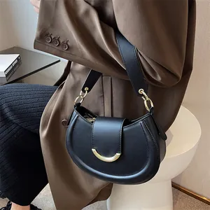 Minimalist black crescent shoulder bag with golden buckle worn with a brown blazer