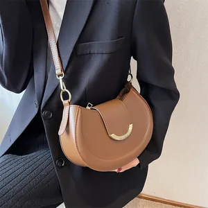 Detail of a brown crescent shoulder bag with a gold crescent buckle worn by a model