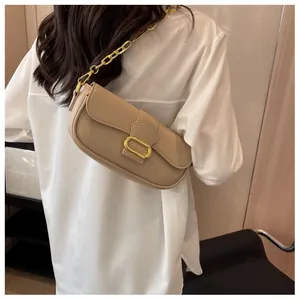Detalle de bolso baguette beige de cuero texturizado con cadena dorada y hebilla