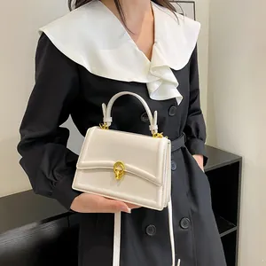 Detail van een minimalistische crèmewitte leren handtas met gouden draaisluiting