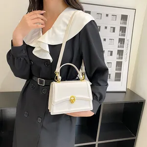 Detail van de crèmekleurige handtas met gouden ovale sluiting en elegant leren handvat