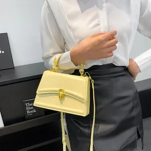Detail van de crèmekleurige vierkante tas met gouden ringgesp op model in het wit