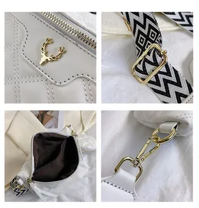 Detail of white quilted crossbody bag with golden deer logo and wide geometric strap