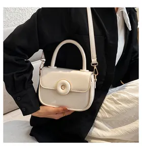 Detail of cream white faux leather crossbody bag with circular magnetic buckle on black blazer