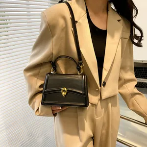 Kleine zwarte matte leren tas met gouden gesp gedragen door model in zakelijke outfit
