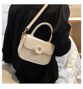 Detail shot of a cream mini crossbody bag with a round buckle and thin shoulder strap