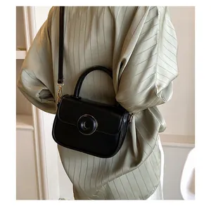 Detail of a chic black leather crossbody bag with a circular metal buckle and top handle