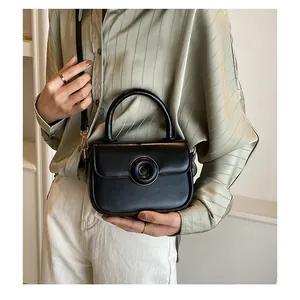 Detail view of small black crossbody bag with large round buckle on a green shirt