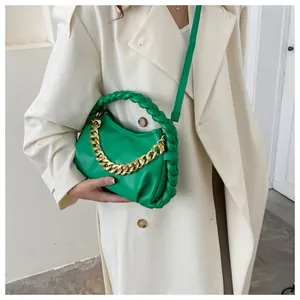 Detail of green crossbody bag with gold chain and woven handle on a white coat