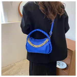 Detail of bright blue chain bag with woven handle and gold hardware on model in black suit